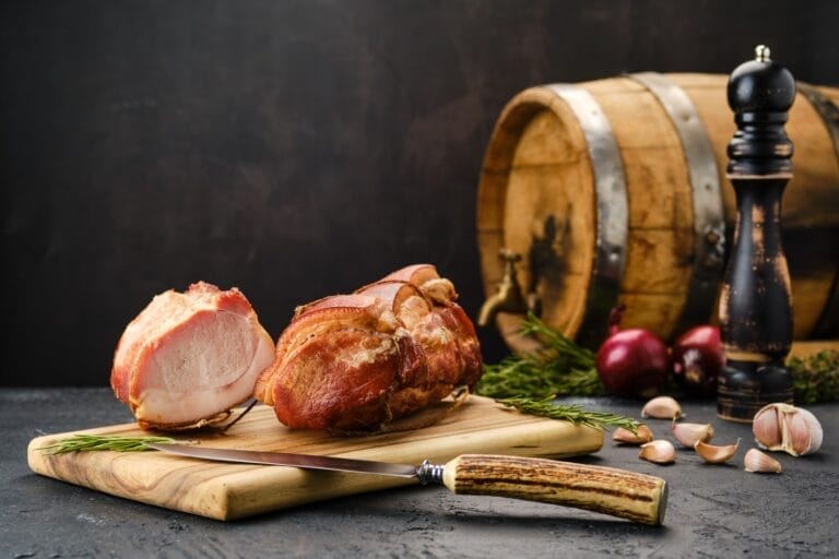 Smoked lamb meat on a wooden cutting board, showcasing tender slices with a rich, smoky texture and garnished with herbs.