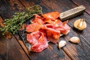 Top view of Spanish cured meat salami, jamon, and choriso sausages arranged on a meat cleaver against a dark wooden backgroun